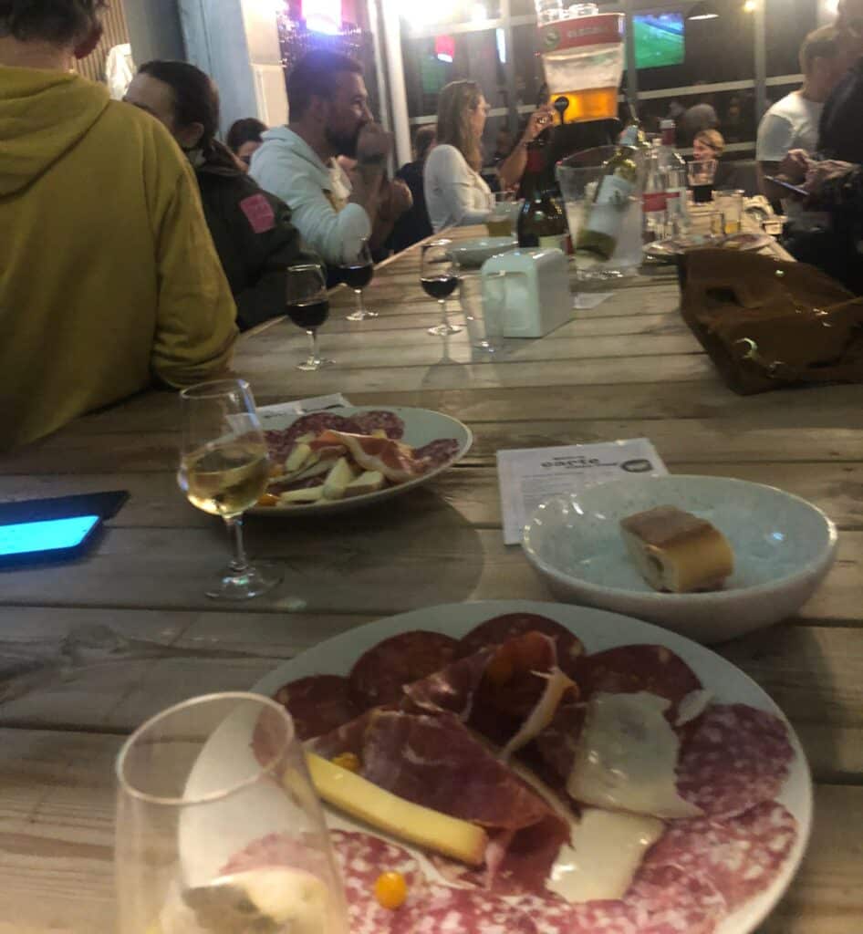 Vue sur les assiettes de charcuterie avec des personnes qui discutent debout, autour d'une grande tablée.